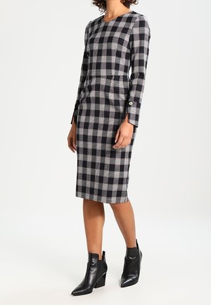 Robe à carreaux noir et blanc avec des manches longues, silhouette ajustée, longueur genoux, dotée d'un col rond et d'accents de boutons dorés sur les manches.