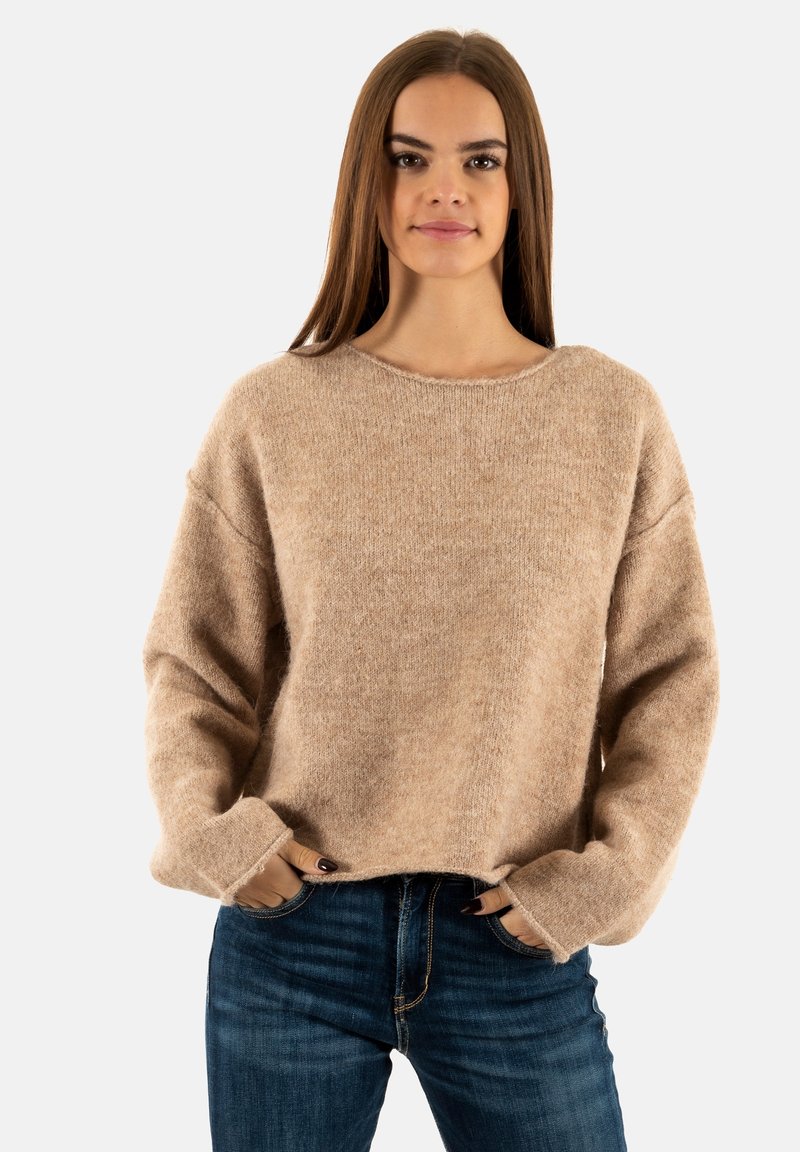 Pull beige doux avec un col rond et des épaules tombantes. Tissu texturé et poignets côtelés. Assorti avec un jean bleu foncé.