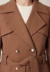 Brązowy płaszcz z mieszanki wełny, dwurzędowy, z dużymi klapami, dwoma metalowymi guzikami oraz pasującym paskiem w talii.