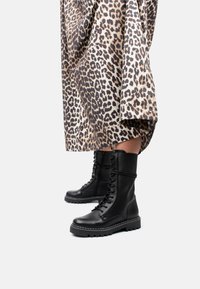 Botas de cuero negro con cordones y suela gruesa, con detalles de costura, acompañadas de una tela con estampado de leopardo.