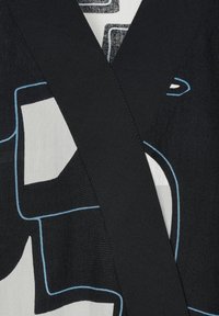 Elemento di abbigliamento in bianco e nero con forme astratte, bordate di blu. La texture sembra liscia, con un dettaglio a fascia nera in contrasto.