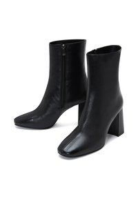Botas negras hasta el tobillo hechas de cuero suave, con cierre de cremallera, puntera afilada y tacón grueso. Diseño elegante con una estética minimalista.