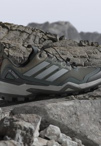 Utomhus vandringsskor i grå och gröna nyanser som vilar på stenig terräng, med en robust sula och snabb snörningssystem.