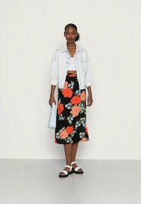 Saia midi preta floral com flores laranja e azuis, combinada com um top cropped branco e uma jaqueta de denim clara oversized. Sandálias brancas e mala azul.