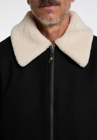 Black jacket with a cream faux shearling collar, zipper closure, and textured fabric. Focus on simplified design and functional details.