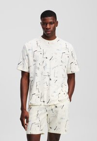 Lysefarvet bomulds T-shirt og shorts sæt med abstrakte sorte og blå skitser. Løs pasform med korte ærmer og rund halsudskæring.