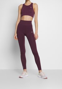 Maroon sportovní podprsenka a legíny. Podprsenka má hluboký výstřih a ribbovaný povrch. Legíny mají síťovinové detaily na kotnících.