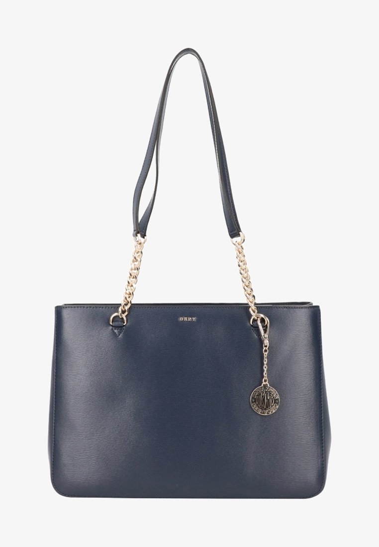 Sac à main en cuir bleu marine avec des anses en chaîne argentée et un pendentif décoratif, présentant une forme structurée et une texture lisse.