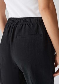 Pantalons noirs légers avec une taille élastique, dotés de deux poches arrière et d'un tissu texturé. Coupe ajustée avec un matériau doux et flexible.