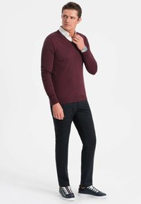 Burgundy v-ringad tröja i stickad kvalitet med ribbade ärmslut, kombinerad med strukturerade svarta byxor och marinblå sneakers med vita snören.