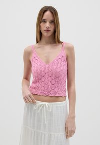 Crop top lavorato a maglia rosa con scollo a V, caratterizzato da un motivo in pizzo e orlo scallopato, abbinato a una gonna bianca fluida con coulisse.
