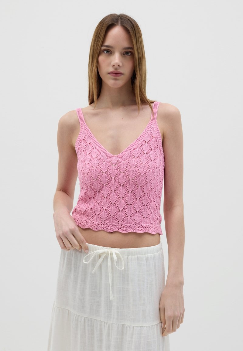 Crop top lavorato a maglia rosa con scollo a V, caratterizzato da un motivo in pizzo e orlo scallopato, abbinato a una gonna bianca fluida con coulisse.