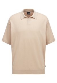 Béžové polo tričko s krátkým rukávem vyrobené z texturovaného materiálu. Má klasický límeček a volný střih. Na bočním švu je decentní logo.