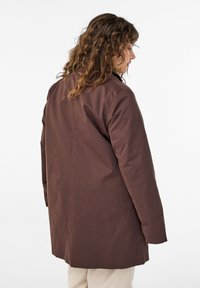 Braune Jacke mit langen Ärmeln und geradem Schnitt, mit glatter Textur und leichtem Glanz. Keine sichtbare Hardware; sauberes Design.