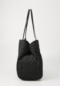 Black quilted tote bag with soft texture, an angular shape, and two long handles. Features a flower pattern and a discreet hardware detail at the top.