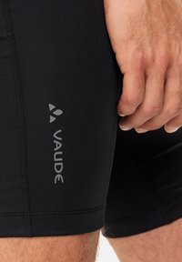 Fekete sportos rövidnadrág, szoros szabással, sima textúrával és lapos varrással; az oldalán egy kis szürke "Vaude" logó található.