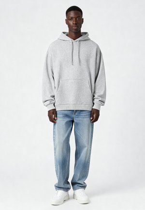 Grijze hoodie met een voorzak in kangoeroestijl, gecombineerd met lichtblauwe denim jeans en witte sneakers, staand tegen een neutrale achtergrond.