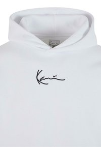 Haut à capuche blanc avec une texture douce, présentant un logo noir en signature sur le devant. La capuche a un design superposé pour un ajustement décontracté.