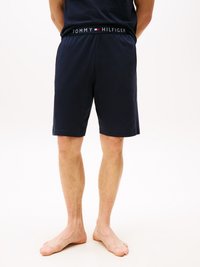 Mann, der marineblaue Tommy Hilfiger-Shorts trägt und von hinten zu sehen ist, barfuß steht er vor einem weißen Hintergrund.