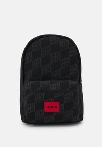 Zaino in tessuto nero con un motivo di logo sottile. Tasca frontale con zip e un prominente patch con logo rosso nella parte inferiore anteriore. Texture liscia.