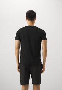 Černé tričko s krátkým rukávem a kulatým výstřihem, vyrobené z hladké látky, v kombinaci s černými šortkami. Minimalistický design bez viditelných log.