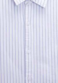 Chemise blanche à fines rayures bleues verticales, avec boutons sur le devant et col classique.