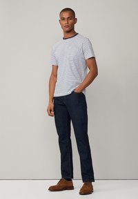 Camiseta a rayas con cuello marino, combinada con jeans azul oscuro y zapatos de cordones marrones. La ropa tiene un corte relajado y un diseño casual.
