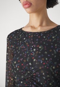 Mustassa verkkopaidassa on pyöreä pääntie, monivärinen kukkakuosi ja rypytetty yksityiskohta vyötäröllä. Läpinäkyvä rakenne.