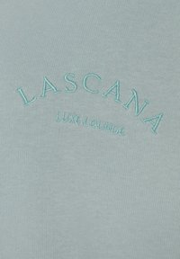 Tessuto blu chiaro con un knit testurizzato, arricchito da ricami delle scritte "LASCANA" e "LUXE LOUNGE" in filo a contrasto. Design morbido e informale.