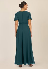 Teal, pitkähelmainen mekko, jossa on lyhyet holahtavat hihat, istuva vyötärö ja takana vetoketju. Pehmeä kangas, jossa on soljuva helma ja hienovarainen kiilto.