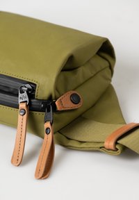 Olivengrüne Tasche mit strukturiertem Außenmaterial, ausgestattet mit schwarzen Reißverschlüssen, Ledergriffen und einem braunen Tragegurt. Sie hat ein elegantes, minimalistisches Design.
