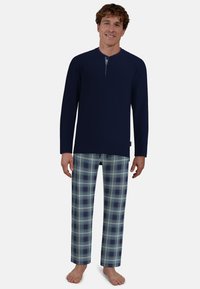 Navy long-sleeve top with henley neckline and button detail, paired with plaid pants in light blue, navy, and beige tones. Feet bare.