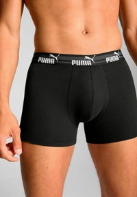 Black cotton boxer shorts with a fitted design, featuring a contrasting Puma logo waistband in white and sleek stitching.