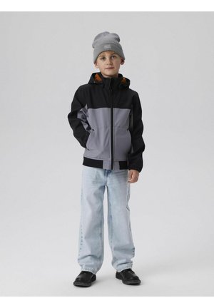Jungenjacke in Schwarz und Grau mit orangefarbenem Akzent, mit Reißverschluss vorne und Kapuze. Getragen mit hellblauen Baggy-Jeans und schwarzen Schuhen.