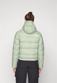 Dik lichtgroene jas met capuchon, met een gewatteerd stiksel en elastische zoom onderaan. Logo zichtbaar op de bovenrug.