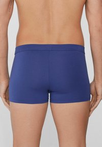 Námořnické modré boxerky s hladkým, elastickým materiálem. Mají široký pas a přiléhavý střih, který ukazuje minimalistický design.