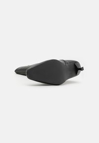 Botte noire en cuir à talons hauts, avec une pointe fine, une texture lisse et une semelle en caoutchouc avec une adhérence texturée pour une meilleure traction.