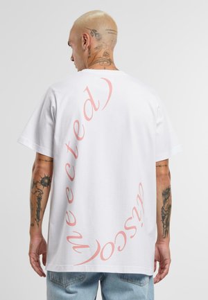 Hvit bomull T-skjorte, oversized passform, med buet rosa tekst på ryggen. Myk tekstur med korte ermer og rund hals.