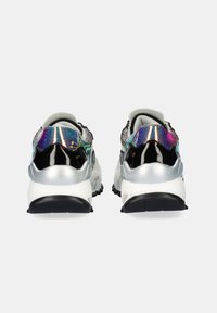 Un par de zapatillas gruesas con suelas blancas, pista negra y acentos brillantes iridiscentes en negro y plata en los talones, mostradas desde atrás.