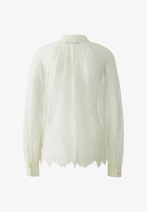 Spitzenbluse in sanftem Elfenbein mit rundem Kragen und langen Ärmeln mit Knopfmanschetten. Durchsichtige Textur mit Blumenmustern und gewelltem Saum.