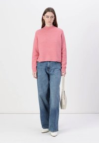 Roza, teksturirana jopica z visokim ovratnikom, kombinirana z širokimi modrimi jeans hlačami. Bele čevlje in svetla torbica dopolnjujejo oblika.