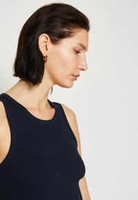 Mornarica rebrasta majica bez rukava s okruglim izrezom, koja ima prilagođeni kroj i široke naramenice. Model je prikazan u profilu.