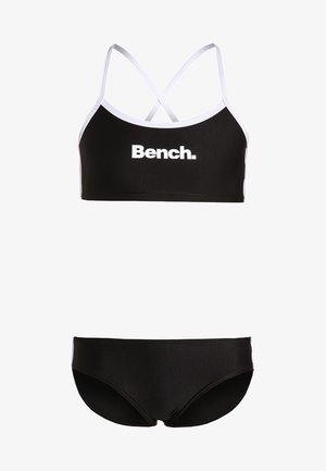 Fekete bikini szett, amely egy fehér díszítésű, rövidített topból és állítható keresztpántos pántokból, valamint illeszkedő, alacsony derekú bikini alsóból áll.