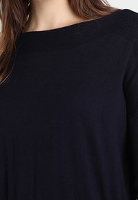 Woman wearing a black, long-sleeve sweater with a wide, boat neckline showing part of the neck and shoulders.
