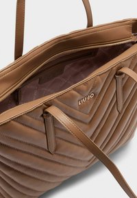 Borsa a tracolla marrone trapuntata con due manici, dotata di chiusura con zip e un logo discreto all'interno. Realizzata in pelle liscia e morbida.