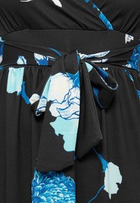 Μαύρο φόρεμα από ύφασμα με μπλε και λευκό λουλουδάτο μοτίβο, με φιόγκο δεμένο στη μέση.