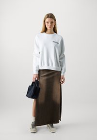 Λευκό φούτερ με κεντημένο λογότυπο, καφέ τζιν μάξι φούστα με πλαϊνό σκίσιμο, ναυτικό μπλε φuzzy τσάντα, γκρι αθλητικά παπούτσια και λευκές κάλτσες.