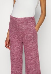 Mysiga vida byxor gjorda av ett melerat tyg i nyanser av rosa, med sidofickor och elastisk midja.