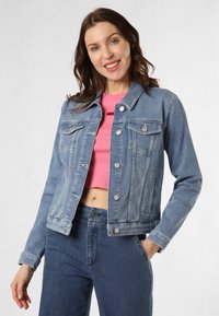 Giacca di jeans blu chiaro con un design classico, tasche frontali, bottoni metallici e una finitura leggermente vissuta, indossata sopra un crop top rosa.