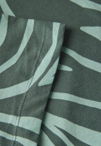 Tessuto a fantasia con strisce turchesi su uno sfondo verde scuro. Include un dettaglio della cucitura, che mette in evidenza la texture morbida del cotone.